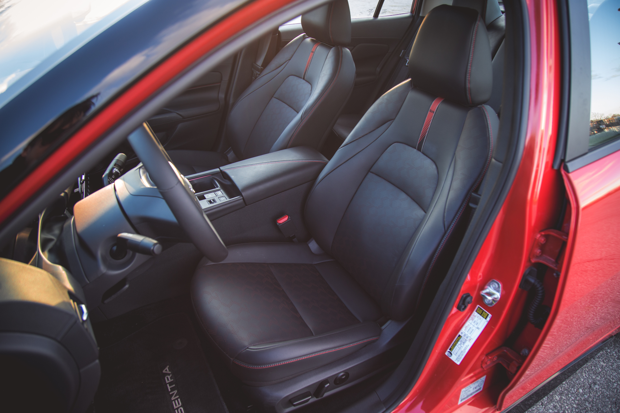 Interior de un automóvil con elegantes asientos de cuero negro con costuras rojas, que muestra un volante y un tablero modernos.
