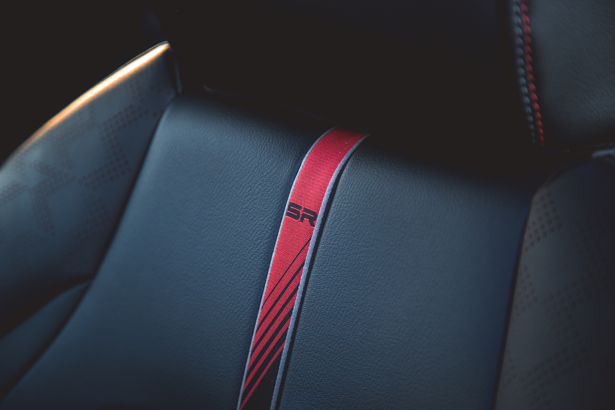 Primer plano de un asiento de automóvil que muestra una superficie de cuero negro con una franja de carreras roja prominente y un logotipo 