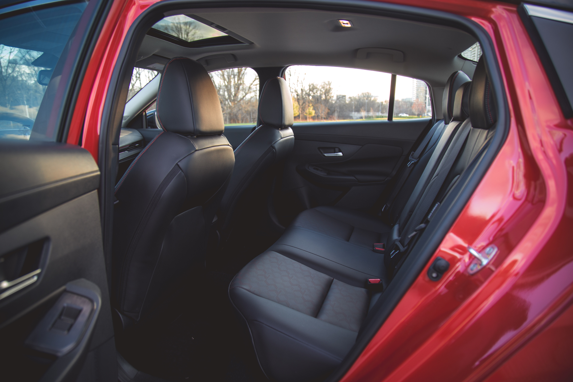 Vista interior del asiento trasero de un coche rojo, con asientos de cuero y diseño espacioso.