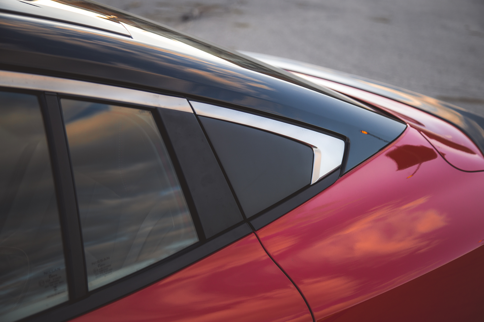 Vista en primer plano de la sección trasera de un automóvil rojo, destacando el diseño elegante y el borde cromado junto a la ventana trasera.