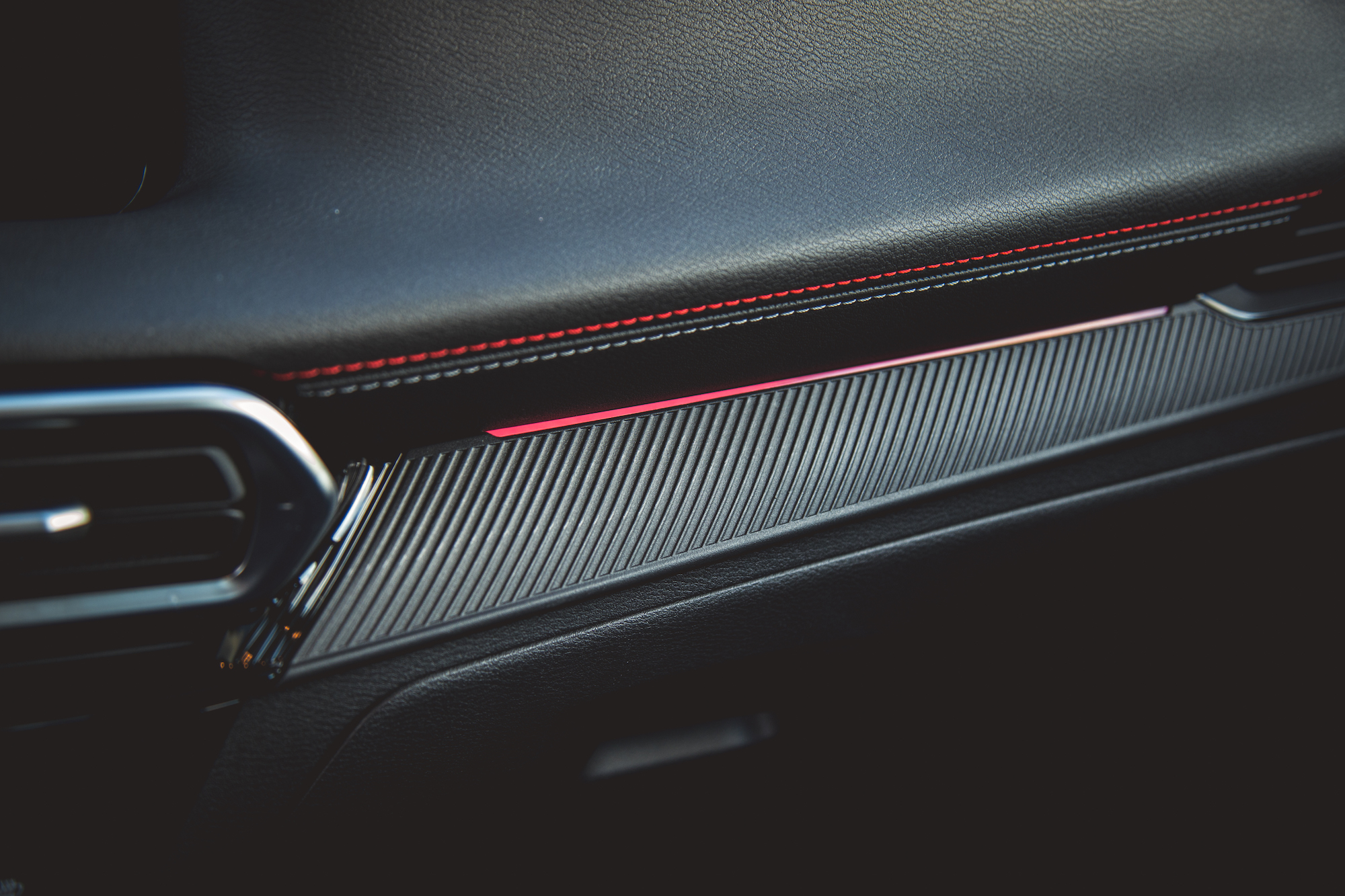 Primer plano del tablero de un automóvil moderno con una elegante superficie negra texturizada con detalles metálicos y costuras rojas.