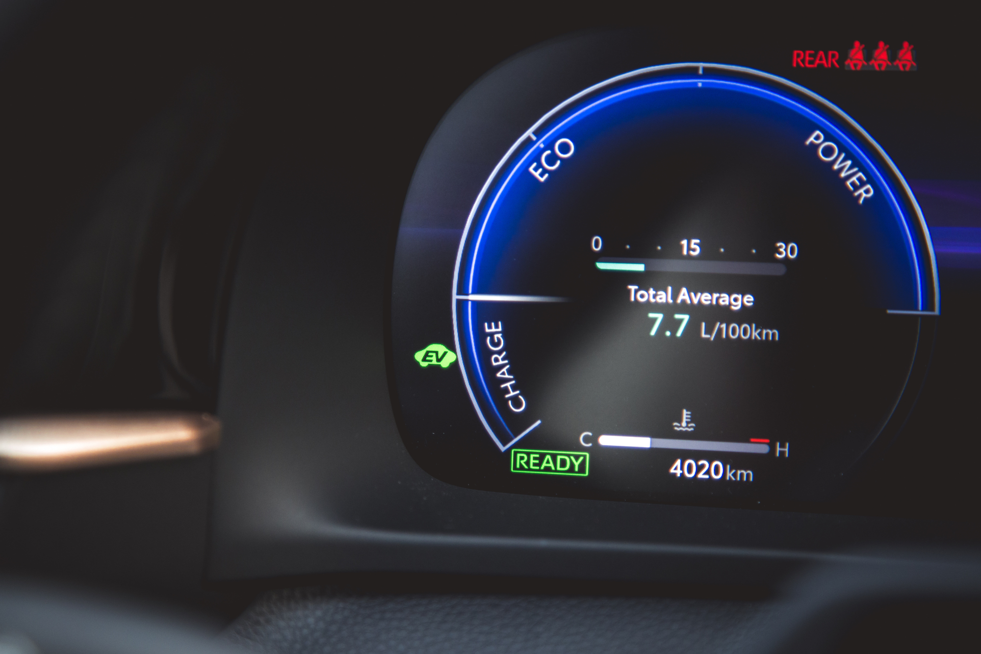Vista cercana de la pantalla del tablero de un automóvil que muestra un consumo promedio de combustible de 7,7 L/100 km, una autonomía de 4020 km y varios indicadores que incluyen el estado eléctrico, de carga y de energía.