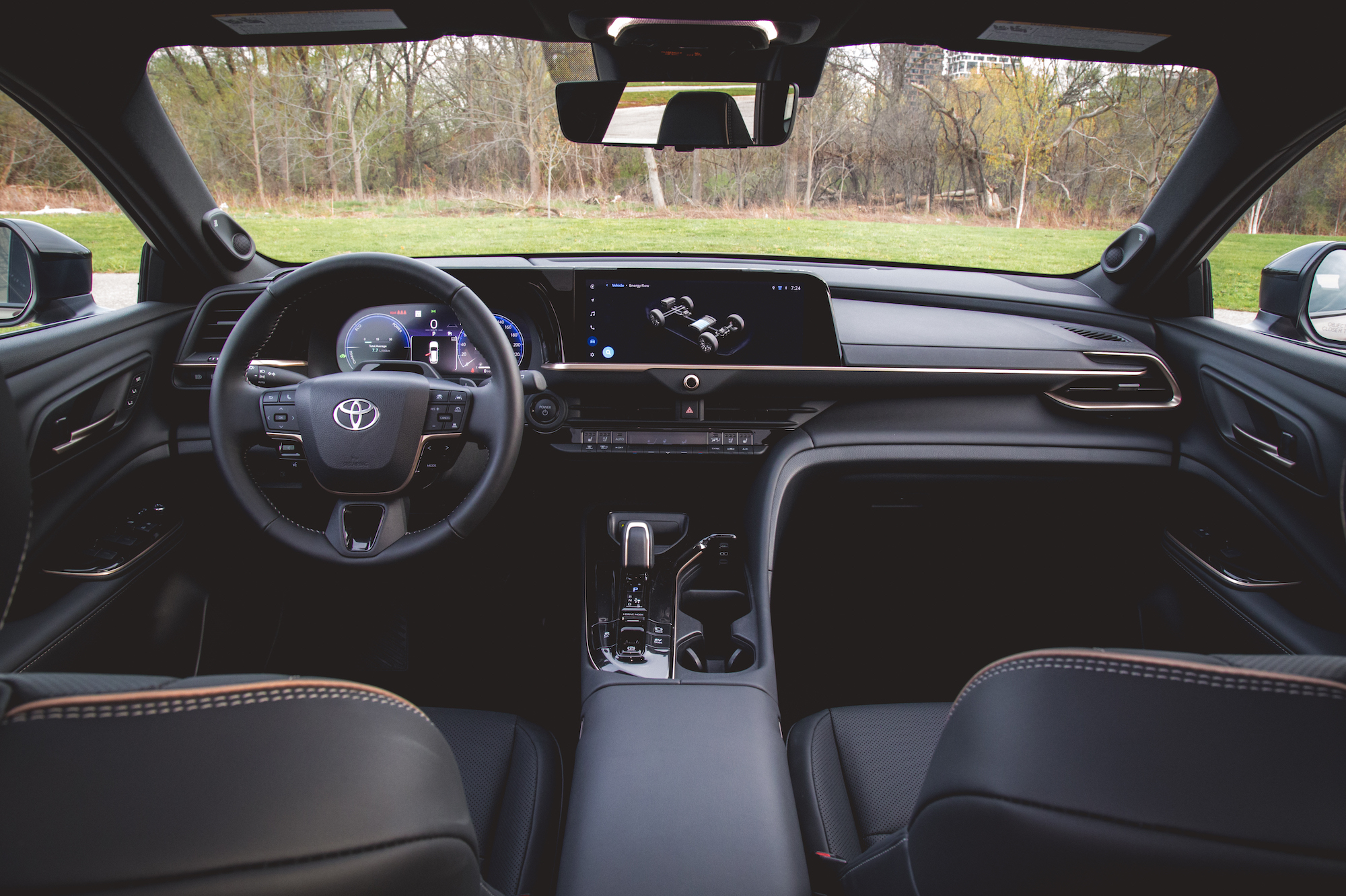 Vista interior de un automóvil moderno con un volante con el logotipo de Toyota, una pantalla de tablero digital y una elegante consola central con controles modernos.