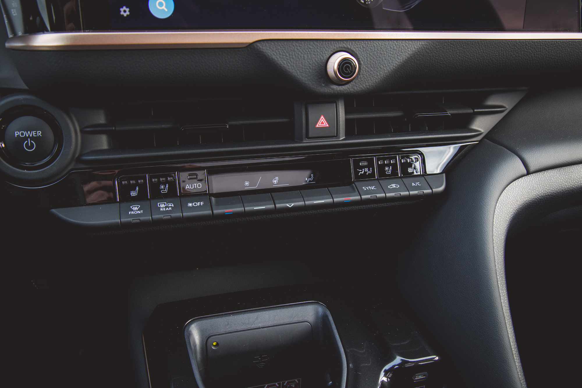 Vista de primer plano de los controles del tablero de un automóvil, que incluye botones de control de clima, un botón de encendido y una interfaz de pantalla táctil.